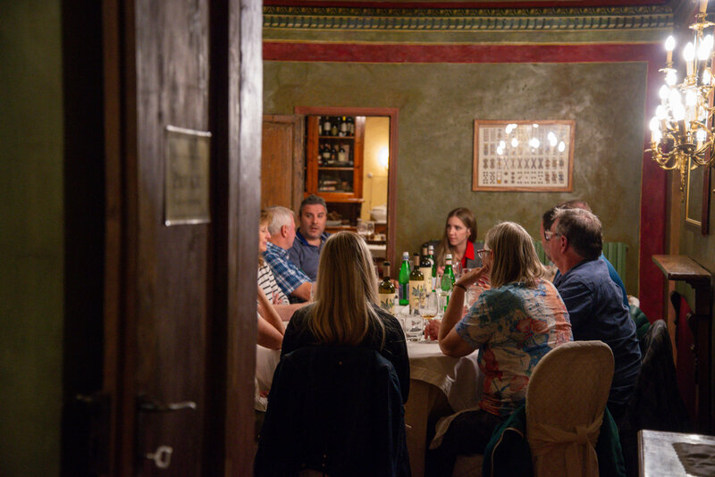 A small group of travelers gathers around a cozy dinner table in a warmly lit Italian restaurant, experiencing a carefully planned food and wine tour in Italy.