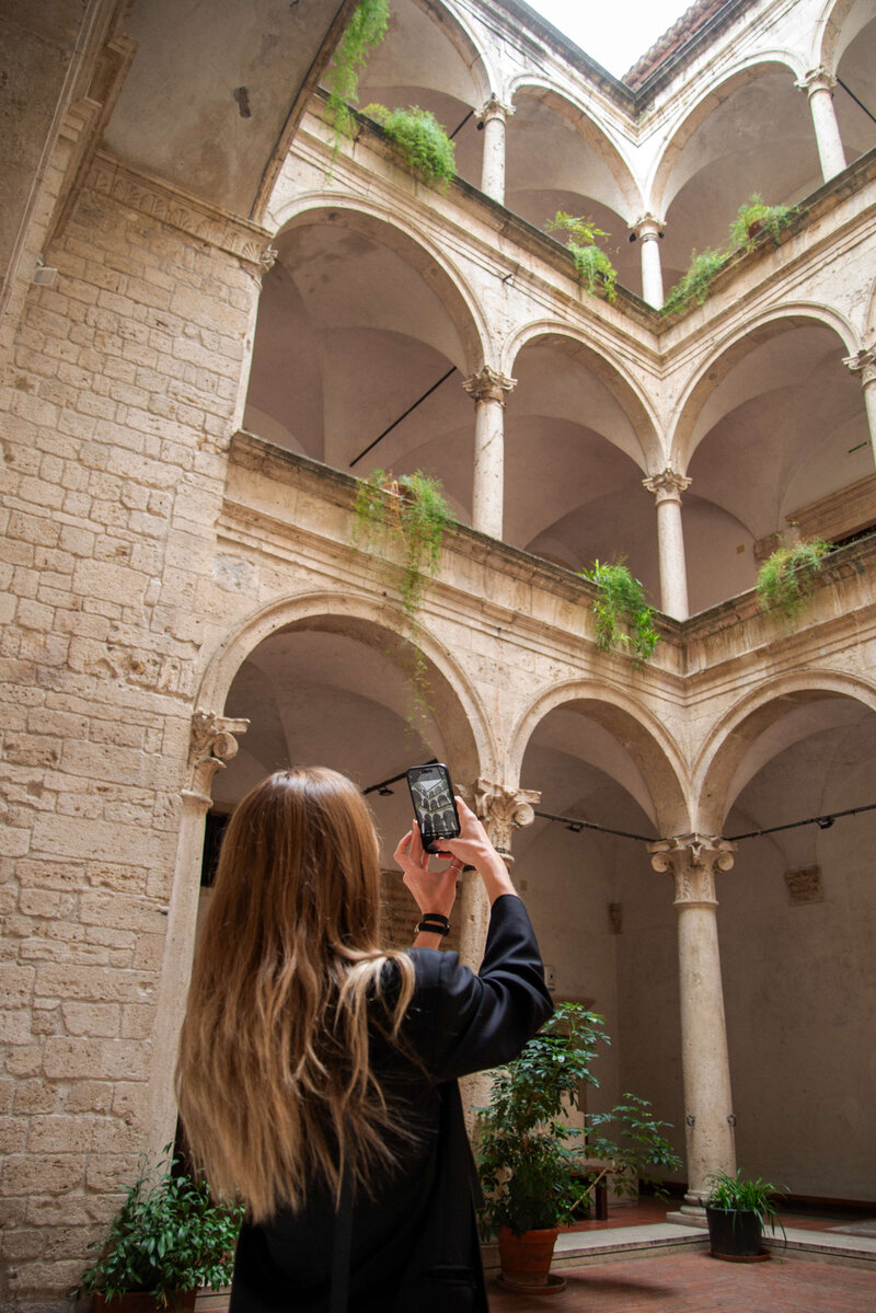 A traveler captures the beauty of an elegant, historic Italian courtyard with grand arches and lush greenery, a highlight of an off-the-beaten-path Italy tour