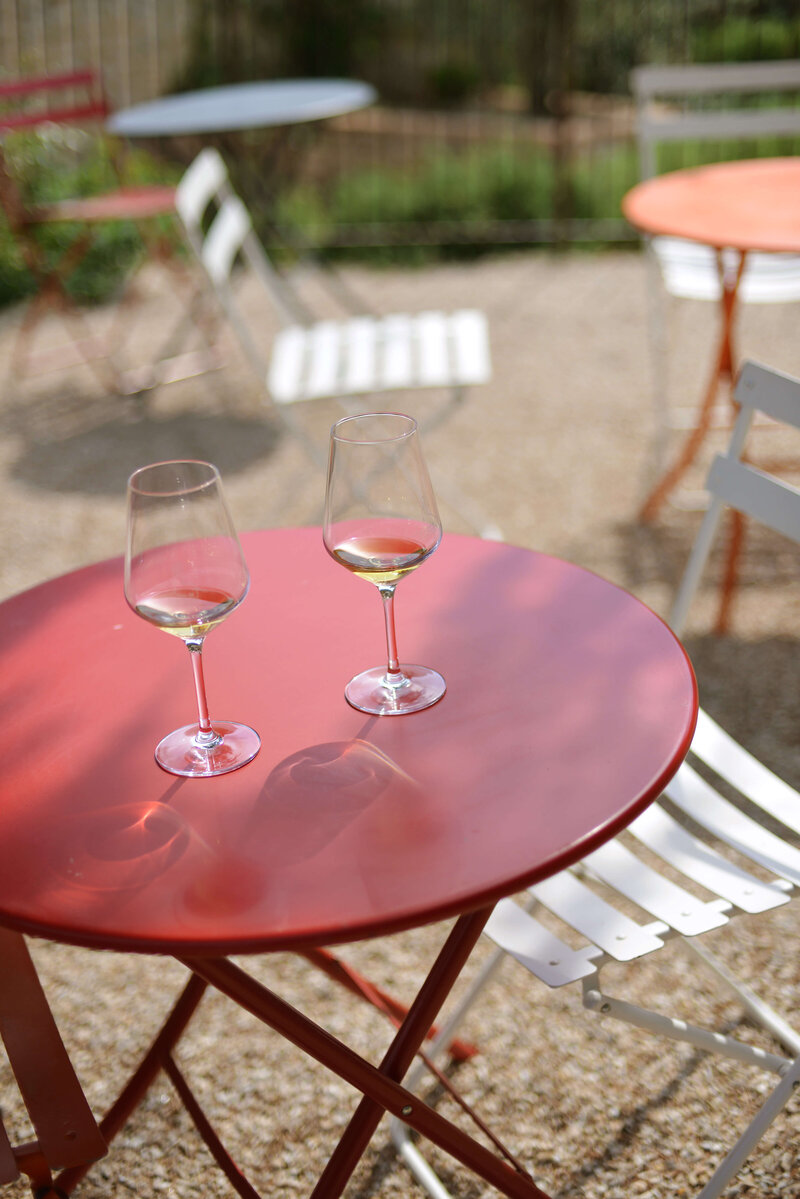 Two glasses of white wine rest on a red bistro table in a peaceful outdoor setting, capturing the relaxed atmosphere of an off-the-beaten-path Italy small group tour.